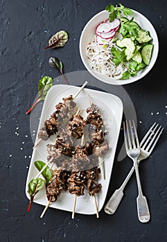 Asian style grilled beef skewers and vermicelli salad on a dark background, top view. Delicious appetizer, tapas