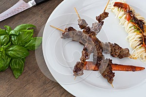 Asian style grilled teriyaki beef skewers on a white plate, top view. Delicious appetizer