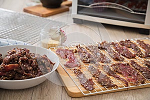 Asian style marinated raw beef strips for homemade jerky dried meat with sesame and chili on dehydrator drying tray, wooden board