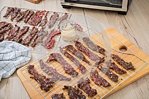 Asian style marinated raw beef strips for homemade jerky dried meat with sesame and chili on dehydrator drying tray, wooden board