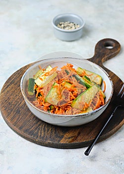 Asian style pickled carrot and fresh cucumber salad sprinkled with sesame seeds in a gray ceramic bowl on a gray concrete