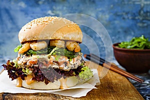 Asian style salmon burger with grilled shrimps, seaweed, lettuce and spicy sriracha mayo sauce served on rustic wooden board.