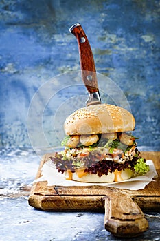 Asian style salmon burger with grilled shrimps, seaweed, lettuce and spicy sriracha mayo sauce served on rustic wooden board.