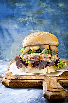 Asian style salmon burger with grilled shrimps, seaweed, lettuce and spicy sriracha mayo sauce served on rustic wooden board.