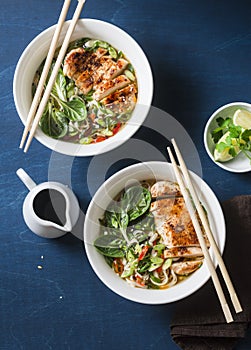 Asian style spicy udon noodle soup with fried chicken on a blue background