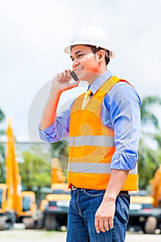 Asian supervisor telephoning on construction site