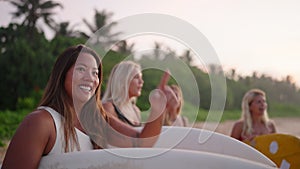 Asian surfer girl holding surfboards talks to friends cheerfully standing on beach at sunrise. Happy biracial female