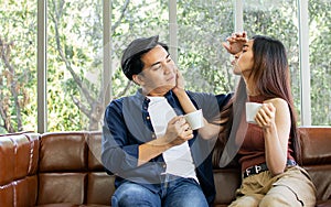 Asian sweet couple boyfriend and girlfriend sitting on sofa in cozy living room at home in morning, drinking coffee together for