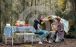 Asian sweet couple man and woman setting tent and camp in forest, playing guitar, adventure backpack traveling together with