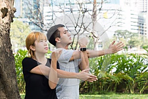 Asian sweet couple warm up their bodies by stretching arms before morning jogging exercise in the park.