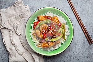 Asian sweet and sour sticky chicken with vegetables stir-fry and rice in ceramic bowl with chopsticks top view, gray