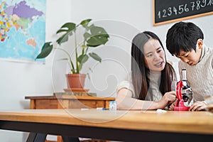 Asian teacher and child boy looking at microscope in science class at preschool - Focus on kid