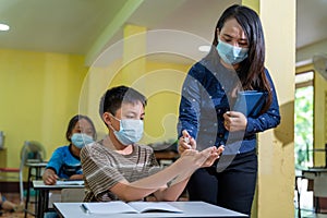 Asian teacher and children with face mask back at school after covid-19 quarantine and lockdown and using antiseptic for