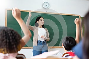 Asian teacher and Diverse Multi ethnic Little Student raising their hands in classroom