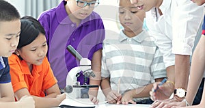 Asian teacher expanding to student in biology class with microscope .