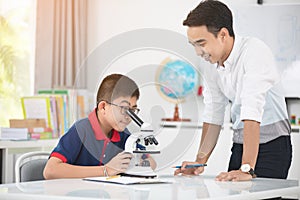 Asian teacher expanding to student in biology class with microscope .