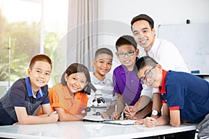 Asian teacher expanding to student in biology class with microscope .