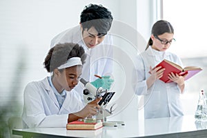 Asian teacher help and guide to African American young scientist child girl use microscope to analysis about plant tissue in