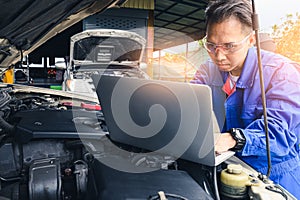 The asian technician analyze the car`s engine graph on laptop computer in the garage. the concept of automotive, repairing, mechan