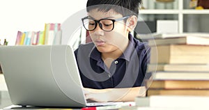 Asian teen boy waring eyeglass and used laptop computer at home, cute boy doing your homework with serious face.