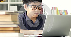 Asian teen boy waring eyeglass and used laptop computer at home, cute boy doing your homework with serious face.