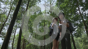 Asian teen brother and sister are searching for directions with mobile phone app while standing in the forest park.