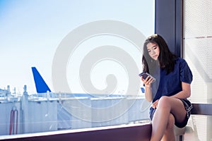 Asian teen girl by airport window looking at smartphone