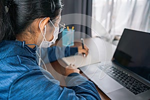 Asian teen girl school pupil wearing headphones distance learning online at virtual class with teacher tutor on laptop by video