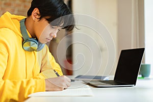 Asian Teen Guy At Laptop Doing Homework Indoors, Side View