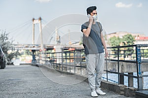asian teen in protective mask talking by smartphone on bridge air