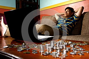 Asian Teen relaxing in front of laptop computer and a stack of coins