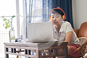 Asian teenage boy getting bored when studying at home wearing headset