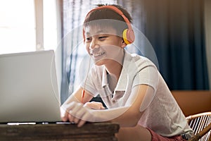 Asian teenage boy studying at home wearing headset and smiling