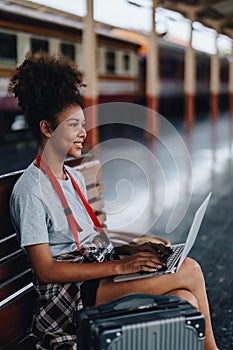 Asian teenage girl african american traveling using computer laptop while waiting for a train at a station.