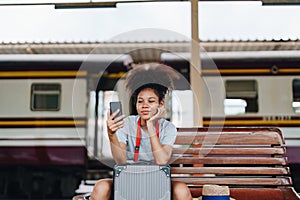 Asian teenage girl african american traveling using smartphone moblie while waiting for a train at a station.