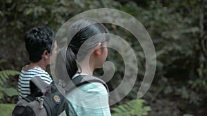 Asian teenage girl with backpack walking with her mother in tropical forest.