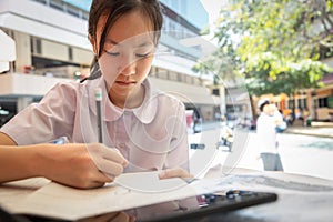 Asian teenage girl student wearing Thai school uniform, writing,taking notes and preparing for the exam reading book,schoolgirl