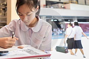 Asian teenage girl student wearing Thai school uniform, writing,taking notes and preparing for the exam reading book,schoolgirl