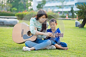 Asian teenage girl teach guitar for the boy with lovingly and fun in the green meadows