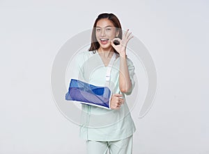 Asian teenage woman wearing a patient gown put on a cast due to injury from an accident showing hand okay with an impressive smile