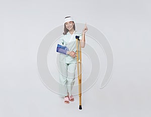 Asian teenage woman wearing a patient gown put on a cast Use a crutch to walk and Bandaged head due to accidental injury standing