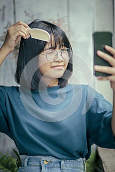 Asian teenager combing forelock hair by comb and smartphone screen