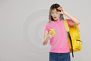 An Asian teenager girl in heart-shaped glasses holds a mobile phone in hands  on gray background.