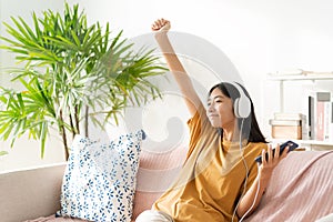 Asian teenager listening to music on smartphone with headset enjoy. raise up hand, Asia woman using mobile phone happy smile relax