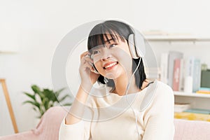 Asian teenager listening to music on tablet with headphone enjoy. Asia woman using computer happy smile while sitting on sofa at