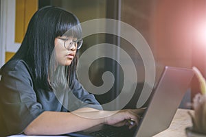 asian teenager sitting in working room and reading message on computer laptop screen