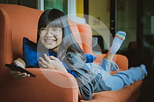 asian teenager smiling with happiness face holding smartphone in hand relax in home living room