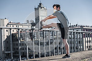 asian teenager stretching legs in protective mask on bridge air