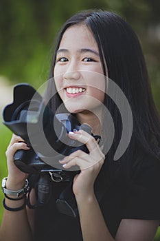 Asian teenager toothy smiling face and holding dslr camera in hand