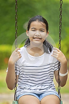 Asian teenager toothy smiling face and sitting on swing in green